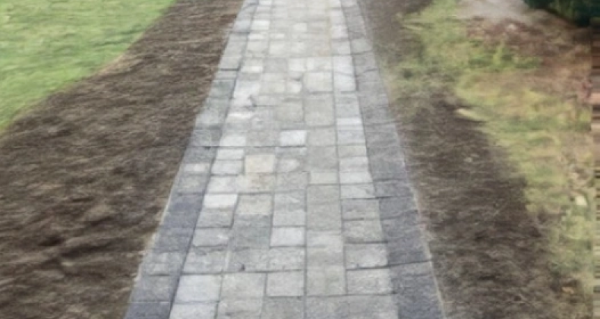 Charming cobblestone walkway winding through a picturesque garden in Brewster, Massachusetts, surrounded by colorful flowers, lush greenery, and quaint garden decor.