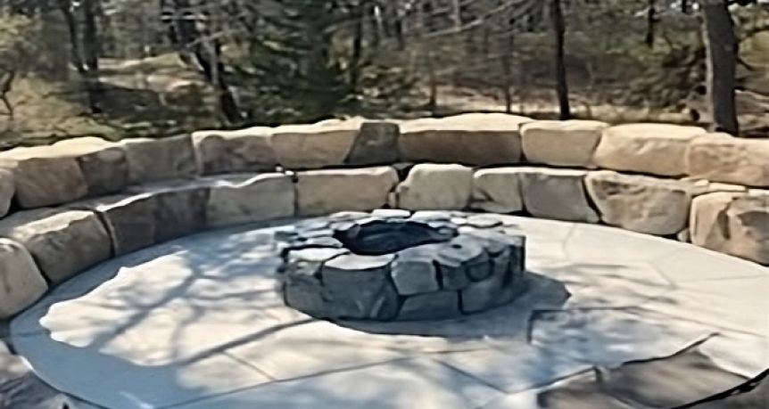 Inviting stone fire pit situated in a beautifully landscaped backyard in Chatham, Massachusetts, surrounded by lush greenery, flowering plants, and comfortable seating area.